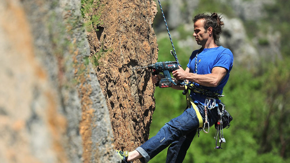 A man in blue clothing is drilling into rocks with a Bosch tool.