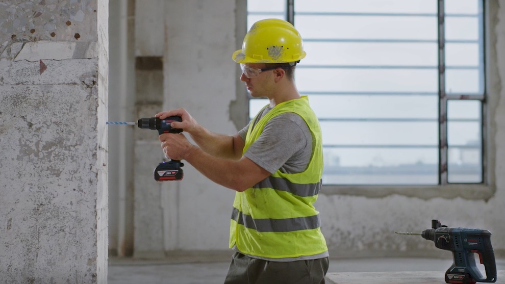 A craftsman is drilling into a wall with a Bosch Professional cordless drill.
