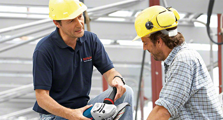 Two men with helmets are discussing a Bosch tool at a construction site.