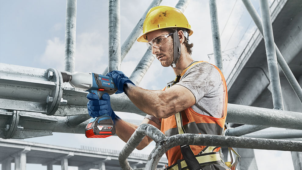 A worker with a yellow helmet is using a Bosch Professional machine.