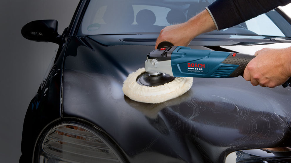 A person is polishing a black car with a blue Bosch GPO 12 CE tool.