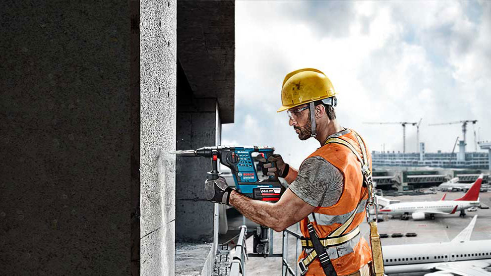 A worker with a Bosch drill on a concrete wall, airport in the background.