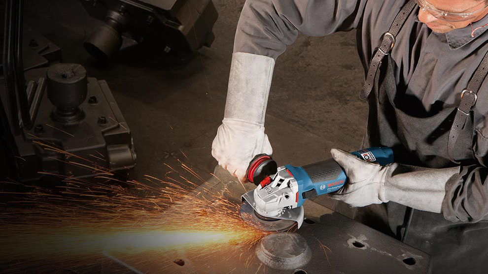 A man with safety goggles is working on metal with a Bosch angle grinder.