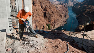 A worker with a helmet is using a jackhammer on the slope of a canyon.