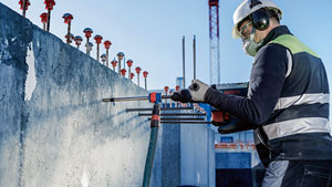 A worker with a helmet is drilling into a concrete wall at a construction site.
