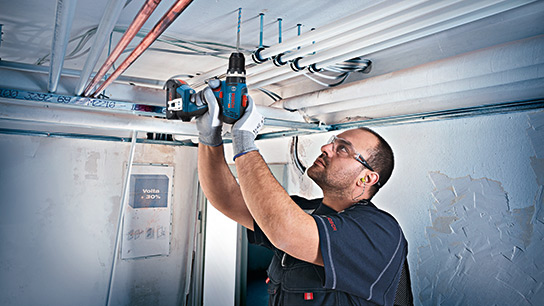 Benefits of 18V System A craftsman is installing pipes with a Bosch Professional cordless screwdriver.