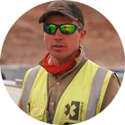 Man in yellow safety vest and sunglasses in front of a construction site.