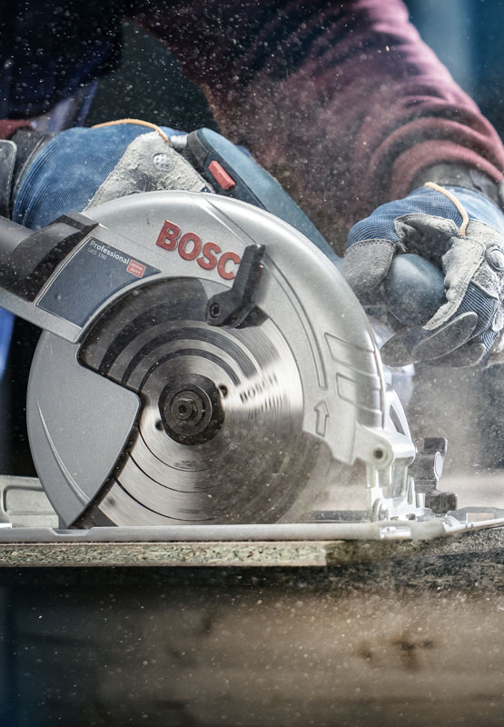 A Bosch Professional circular saw is being used on wood, dust is swirling up.
