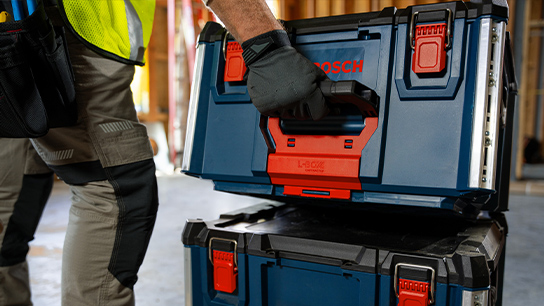 A craftsman lifts a blue toolbox with a red handle onto another box.