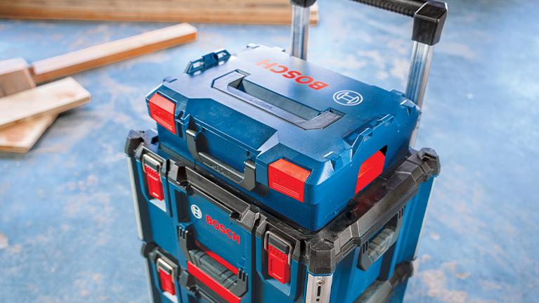 A blue toolbox from Bosch is standing on another box, on a wooden floor.