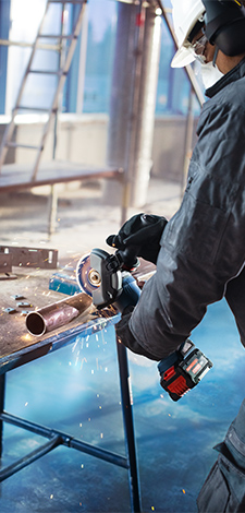 A worker in protective clothing is using a Bosch Professional angle grinder at a table. Sparks are flying.